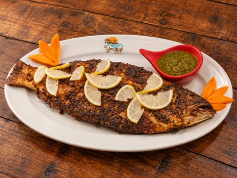 Grilled whole fish with lemon, carrot garnish and green sauce on a Dwipantor-branded plate at Charcoal Restaurant