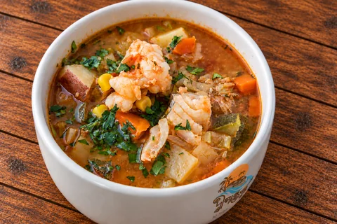 Seafood soup with prawns and vegetables in a Dwipantor-branded white bowl on a wooden table at Charcoal Restaurant