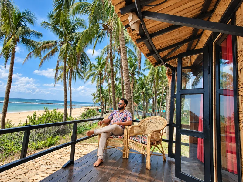 A guest relaxing on the sea-view balcony of a Duplex Villa at Dwipantor Beach Resort, surrounded by coconut palms