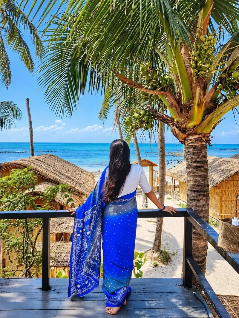 A guest looking towards the sea between palm trees and cottages at Dwipantor